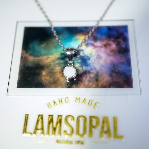 A silver-toned pendant necklace with a round white stone is displayed on a card featuring a colorful galaxy print, with the brand name 'LAMSOPAL' printed in gold below.