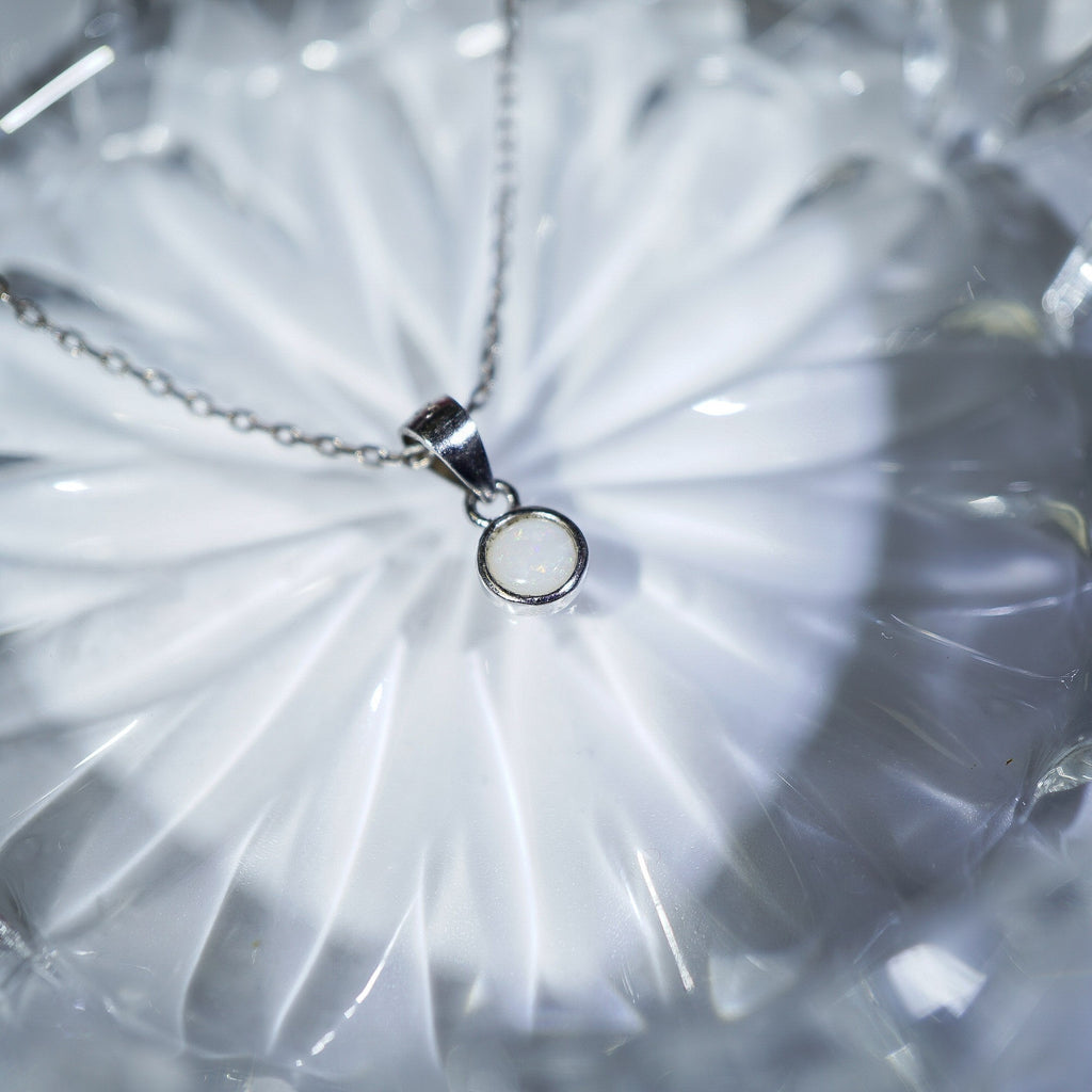 A silver necklace with a minimalist circular pendant resting on a textured, translucent white glass dish.