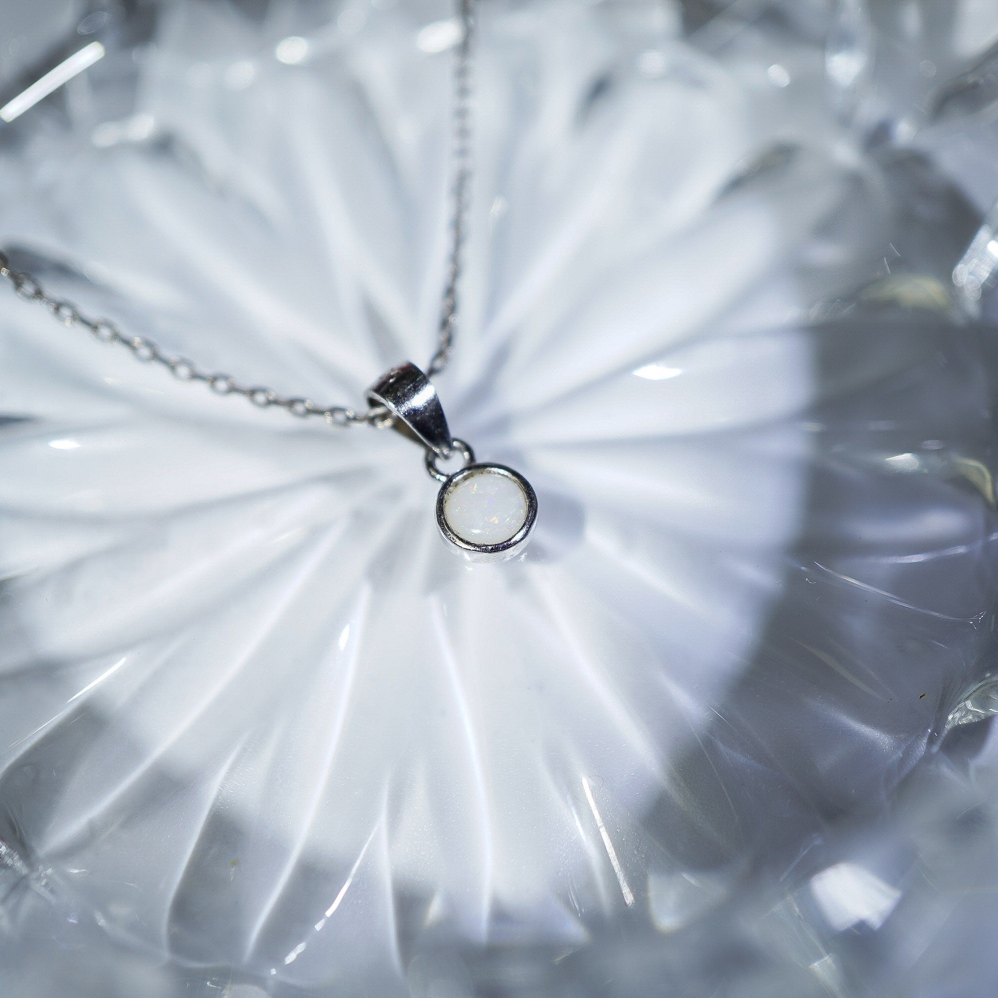A silver necklace with a minimalist circular pendant resting on a textured, translucent white glass dish.