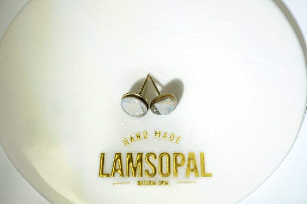 A pair of gold-toned stud earrings with round, iridescent shell-like cabochons resting on a white circular display card printed with the brand name 'LAMSOPAL'.