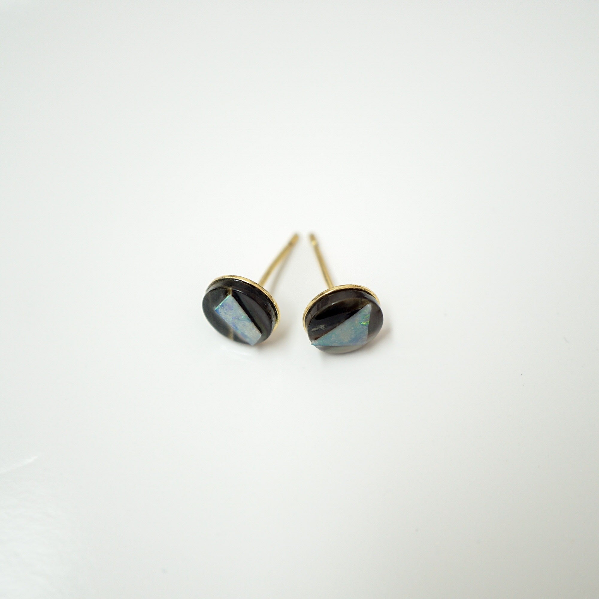 A pair of gold stud earrings with oval faceted dark iridescent stones, displayed on a clean white background.