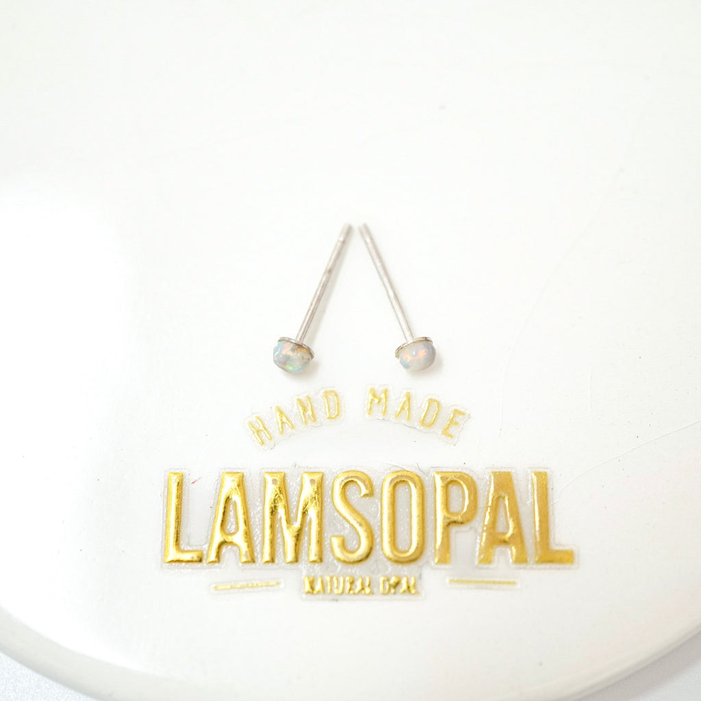A pair of silver-toned stud earrings with round, iridescent opal-like beads, displayed above a gold foil logo that reads 'HAND MADE LAMSOPAL NATURAL DEG'.