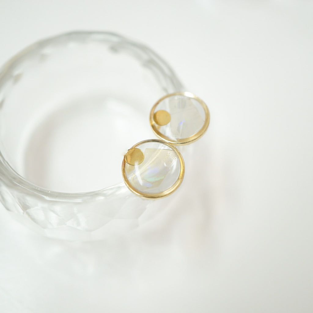 A clear textured glass or acrylic bangle bracelet with two gold-tone circular bezel settings holding iridescent round cabochon stones, photographed on a clean white background.