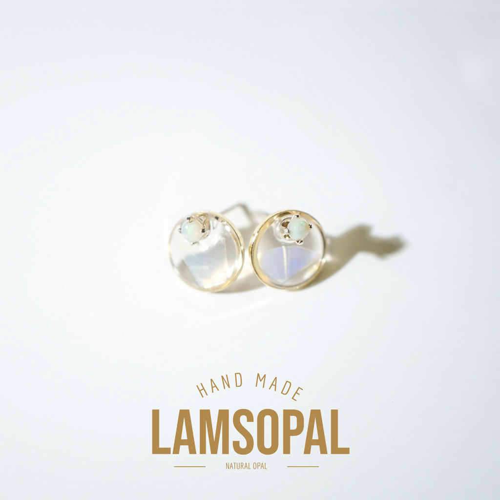 A pair of gold stud earrings with round iridescent opal cabochons, displayed on a clean white background with a soft shadow. Below the earrings, the text 'HAND MADE LAMSOPAL NATURAL OPAL' is printed in gold.