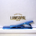 A metallic blue clip-style accessory resting on a white surface in front of a white textured background with gold text reading 'HAND MADE LAMSOPAL NATURAL OPAL'.