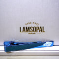 A blue Lamsopal tie clip placed on a white surface in front of a textured white background with gold 'LAMSOPAL' branding.