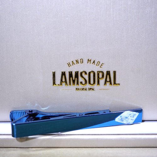 A blue Lamsopal tie clip placed on a white surface in front of a textured white background with gold 'LAMSOPAL' branding.