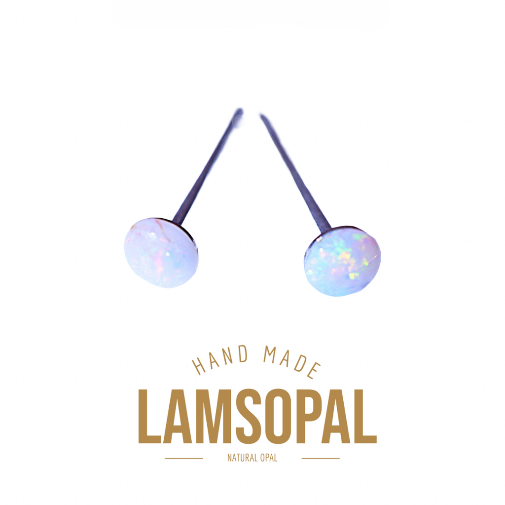 Two Lamsopal natural opal stud earrings with round iridescent opal discs on dark metal posts, displayed above gold-colored text reading 'HAND MADE LAMSOPAL NATURAL OPAL' on a plain white background.
