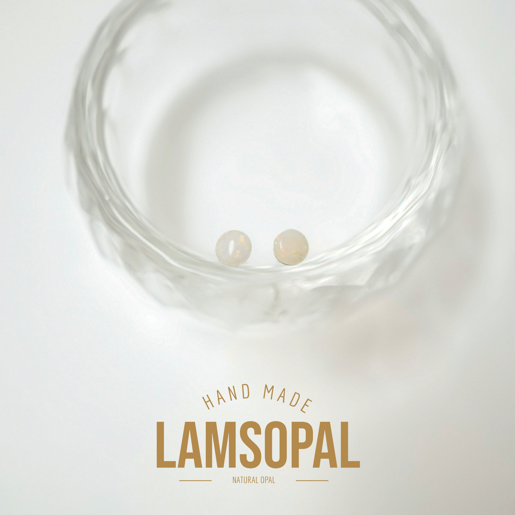 Two small natural opal gemstones displayed inside a clear textured glass bowl, with a text overlay at the bottom reading 'HAND MADE LAMSOPAL NATURAL OPAL' on a white background.