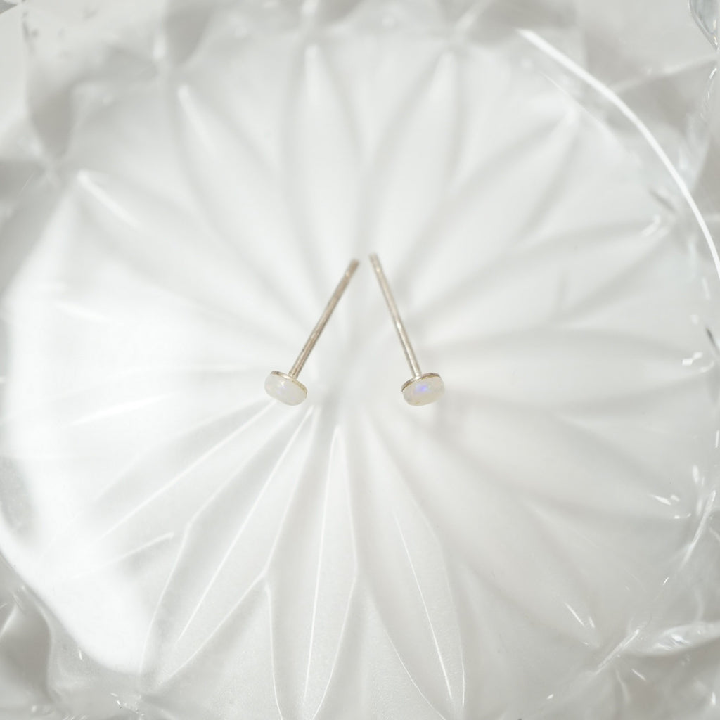 Two small silver stud earrings with oval white cabochon stones, displayed on a textured white glass plate.