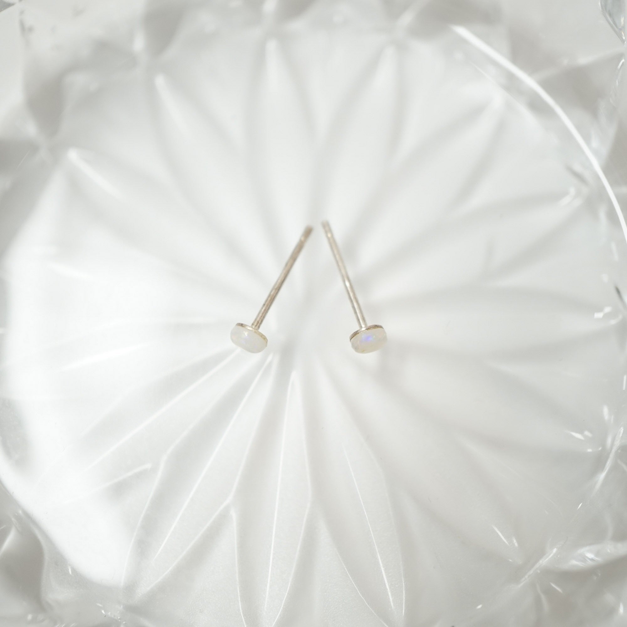 Two small silver stud earrings with oval white cabochon stones, displayed on a textured white glass plate.