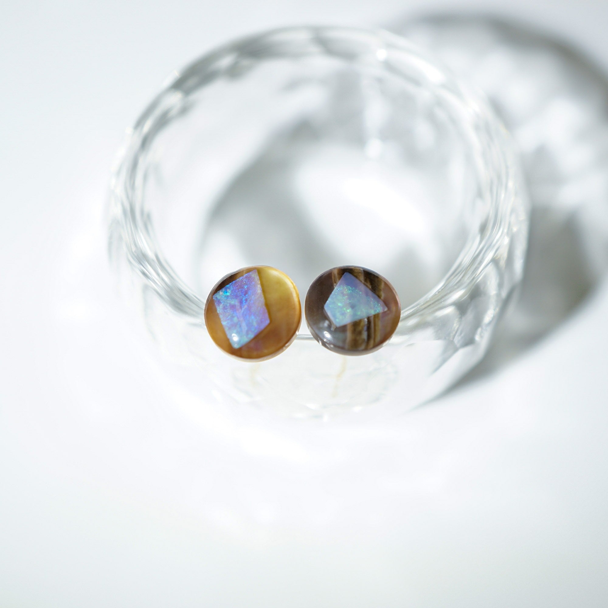 A pair of handmade Lamsopal natural opal stud earrings on glass