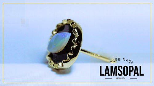 A gold ring with a natural opal gemstone, featuring a wavy bezel setting and a post, shown against a light blue background with a gold border. The text 'HAND MADE LAMSOPAL' is visible in the bottom right corner.