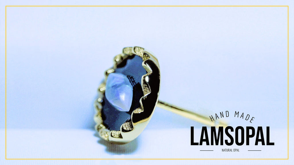 A gold-toned Lamsopal stud earring with a scalloped bezel setting holding a round natural opal gemstone, shown on a light blue background with a brand logo overlay.