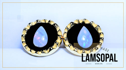 A pair of round stud earrings with scalloped gold-tone edges, black centers, and teardrop-shaped iridescent blue-white opal gemstones. The image includes a text overlay reading 'HAND MADE LAMSOPAL NATURAL OPAL' on a light blue background.
