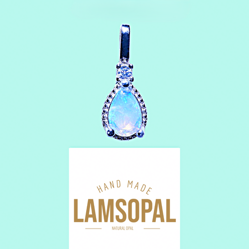 A teardrop-shaped Lamsopal pendant with a light blue iridescent center and silver-toned bezel set with small clear stones, shown above a white card printed with the brand name LAMSOPAL on a light aqua background.