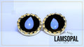 A pair of Lamsopal natural opal stud earrings with teardrop-shaped light blue opal centers set in a gold bezel with a black background, shown on a light blue background with a gold border.