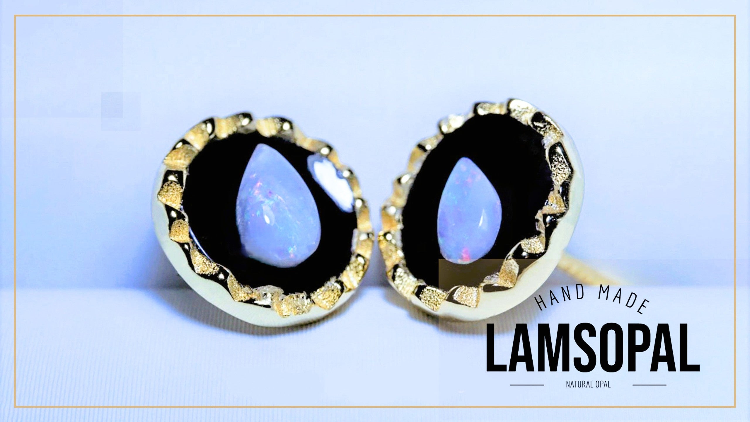 A pair of Lamsopal stud earrings featuring teardrop-shaped natural opal stones with a blue and white iridescent sheen, set in a black background and a textured gold bezel. The image includes a 'HAND MADE LAMSOPAL' text overlay on the bottom right.
