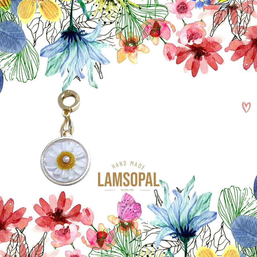 A handmade daisy pendant charm with a gold-tone clasp and ring, featuring a white center with yellow and blue watercolor floral illustrations in the background and the brand name 'LAMSOPAL' printed below.