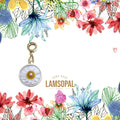 A handmade daisy pendant charm with a gold-tone clasp and ring, featuring a white center with yellow and blue watercolor floral illustrations in the background and the brand name 'LAMSOPAL' printed below.