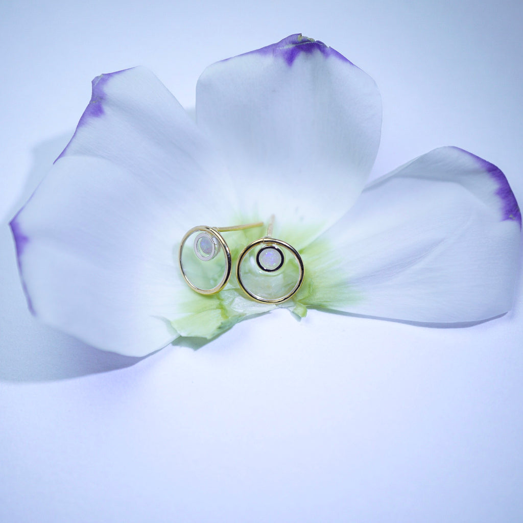 A pair of gold-toned ring holders or glasses stands on the center of a white flower with purple-tipped petals against a soft light blue background.