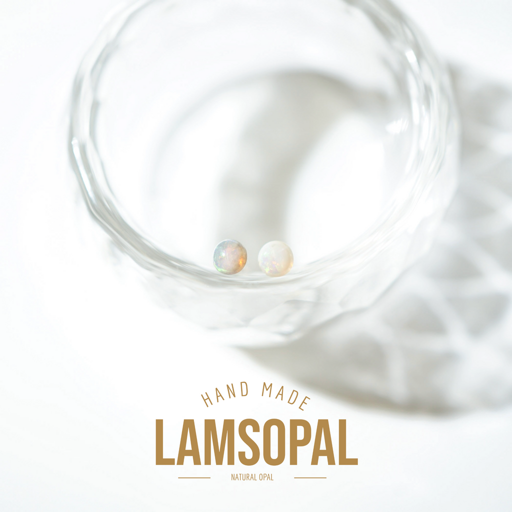 Two small round natural opal stud earrings resting inside a clear faceted glass bowl, with a soft shadow and the text 'HAND MADE LAMSOPAL NATURAL OPAL' below on a white background.