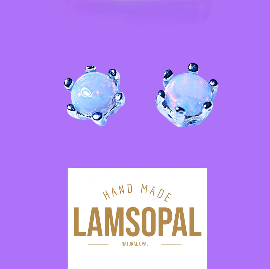 Two small round light blue opal gemstone stud earrings with silver prongs, displayed on a purple background above a white label that reads 'HAND MADE LAMSOPAL NATURAL OPAL'.