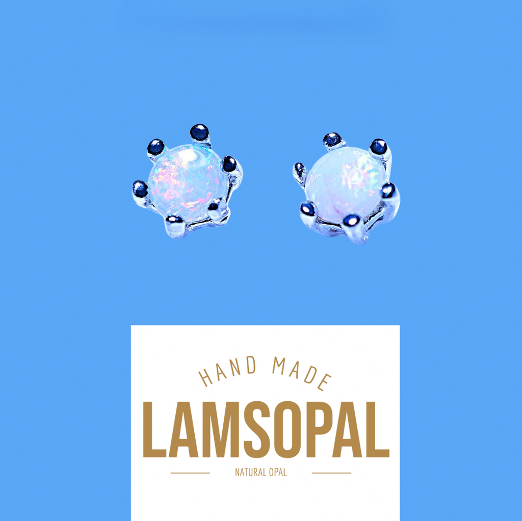 Two handmade Lamsopal natural opal stud earrings with silver settings and small dark blue beads, shown above a white label with the brand name 'LAMSOPAL' on a solid blue background.