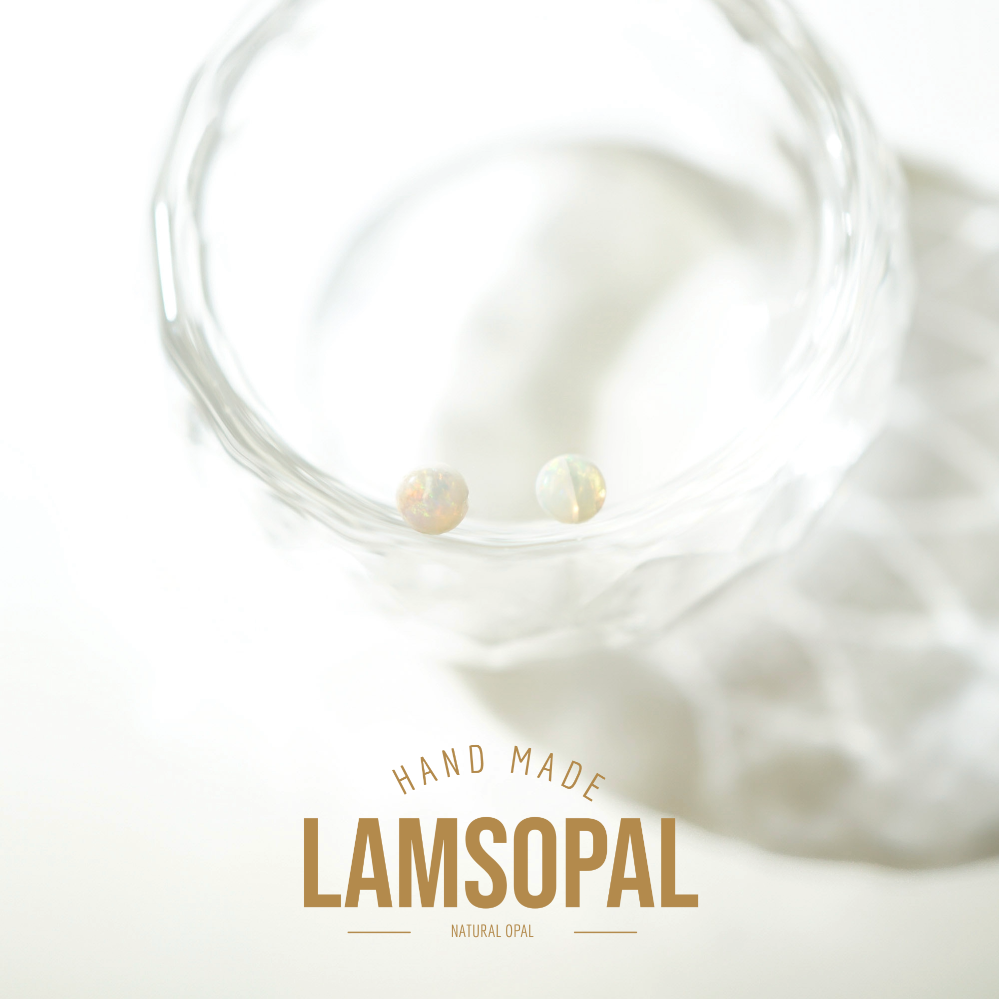 Two small round natural opal gemstones resting inside a clear textured glass bowl, with a soft-focus background and the text 'HAND MADE LAMSOPAL NATURAL OPAL' at the bottom.