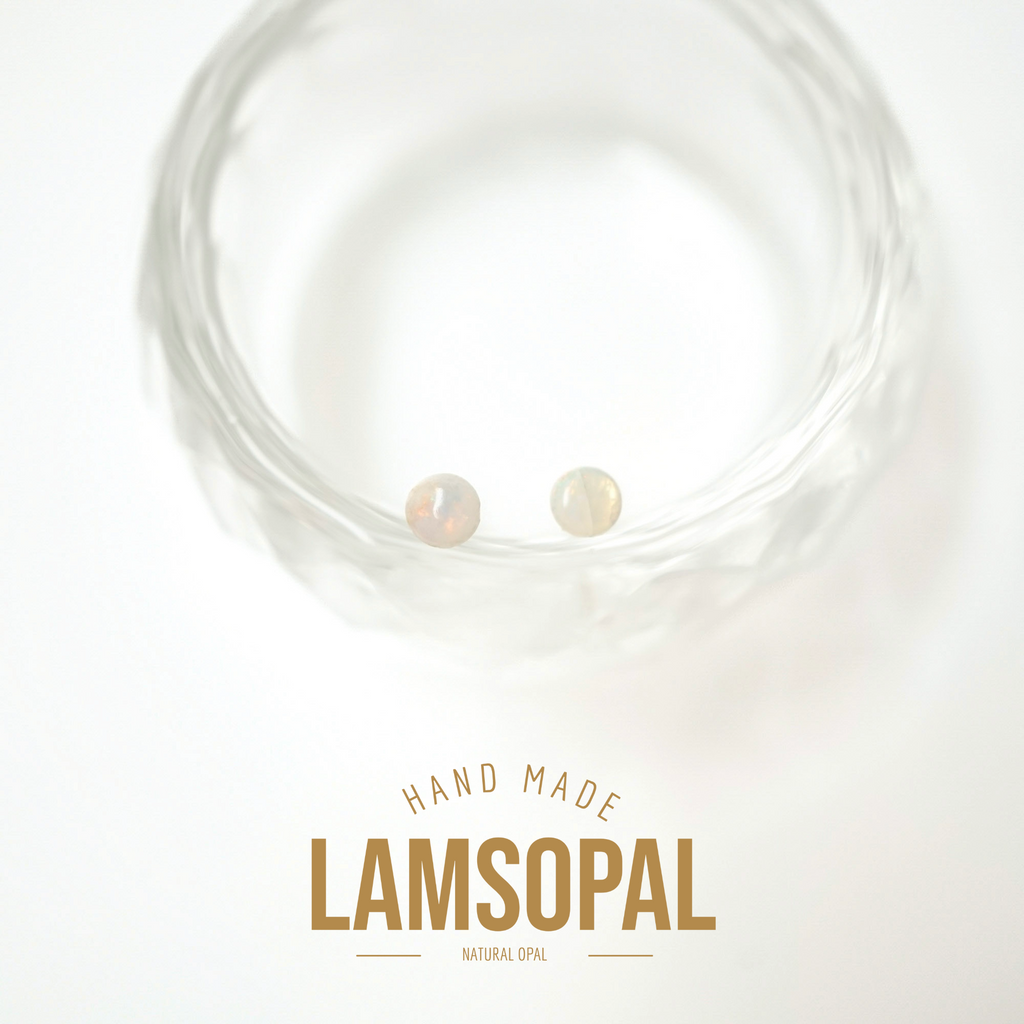 Two small natural opal gemstones displayed inside a clear textured glass bowl, with text below reading 'HAND MADE LAMSOPAL NATURAL OPAL' on a white background.
