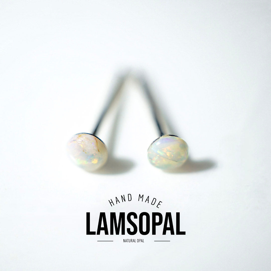 A pair of Lamsopal natural opal stud earrings with round iridescent white opal cabochons on black posts, displayed on a clean white background with a brand logo overlay at the bottom.