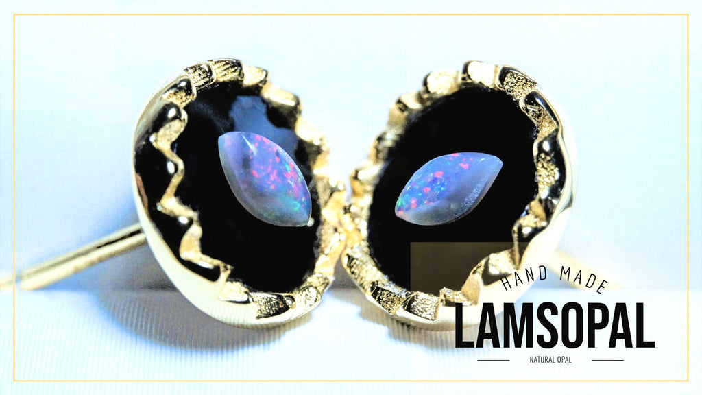 A pair of gold-toned stud earrings with teardrop-shaped natural opal gemstones set in black bezel settings, shown on a light blue background with a 'HAND MADE LAMSOPAL NATURAL OPAL' text overlay.