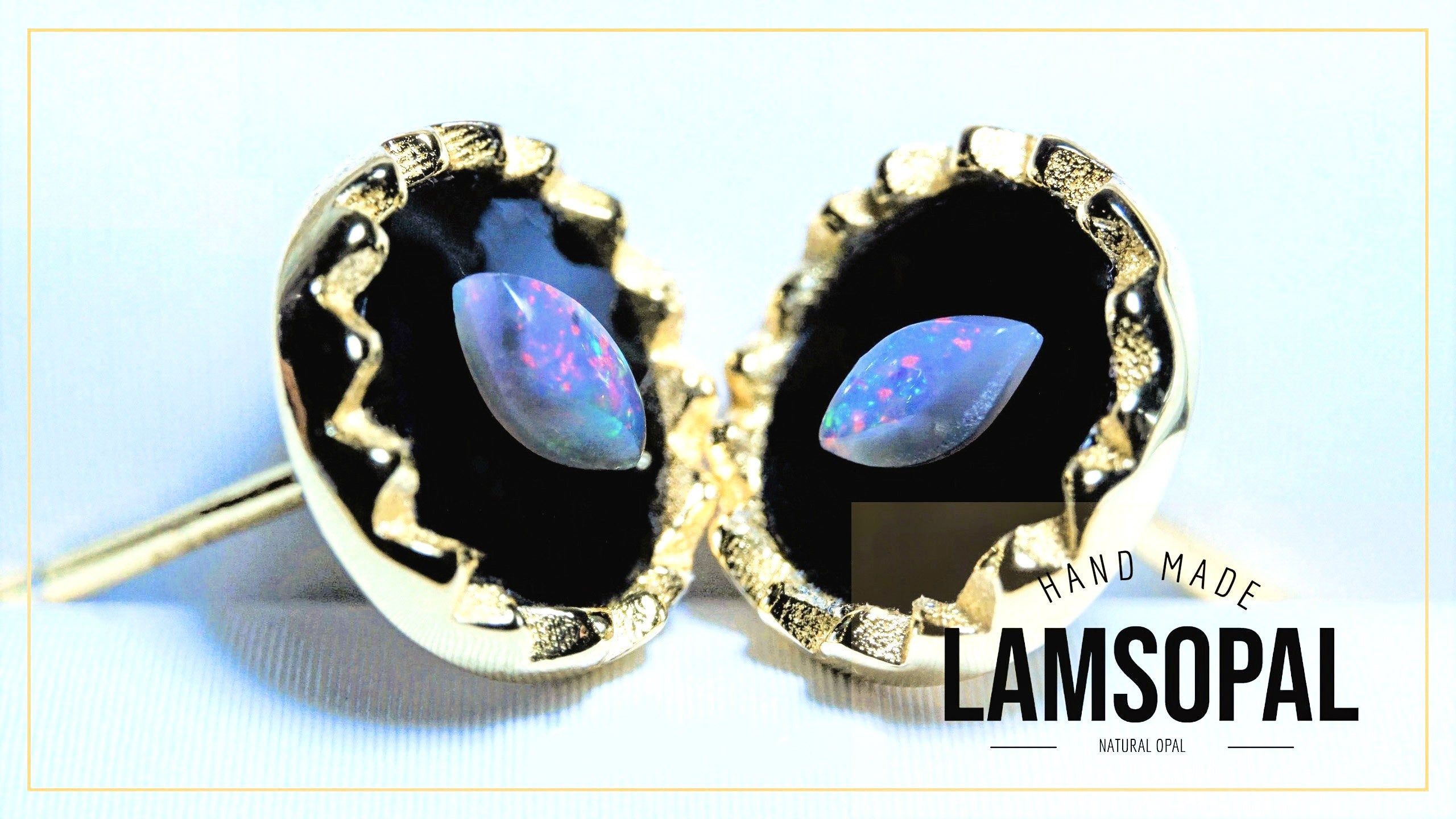 A pair of gold-toned stud earrings with teardrop-shaped natural opal gemstones set in black bezel settings, shown on a light blue background with a 'HAND MADE LAMSOPAL NATURAL OPAL' text overlay.