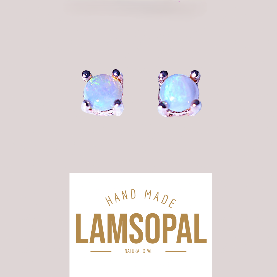 A pair of handmade Lamsopal natural opal stud earrings in silver-toned metal prong settings, shown above a white label with the brand name 'LAMSOPAL'. The opal stones exhibit a milky white color with subtle blue and green iridescent flashes.
