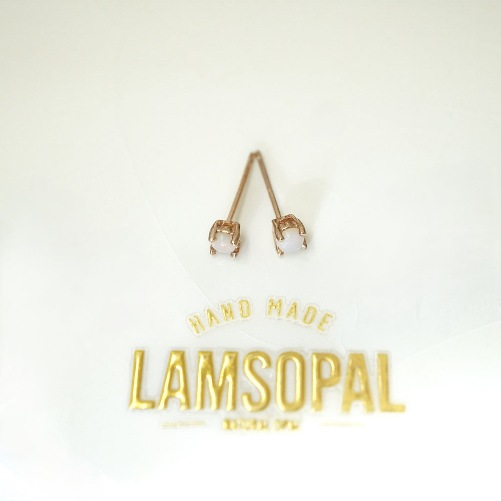 A pair of rose gold stud earrings with clear gemstones in prong settings, displayed on a white background above gold foil branding that reads 'HAND MADE LAMSOPAL'.