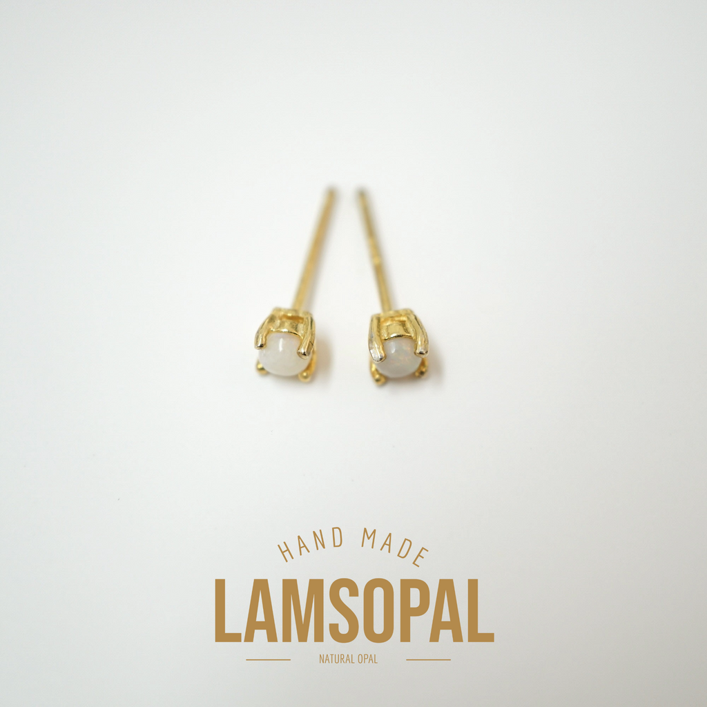 A pair of gold post earrings with oval white opal gemstones, displayed on a clean white background with a gold 'LAMSOPAL' brand logo and 'HAND MADE' text below.
