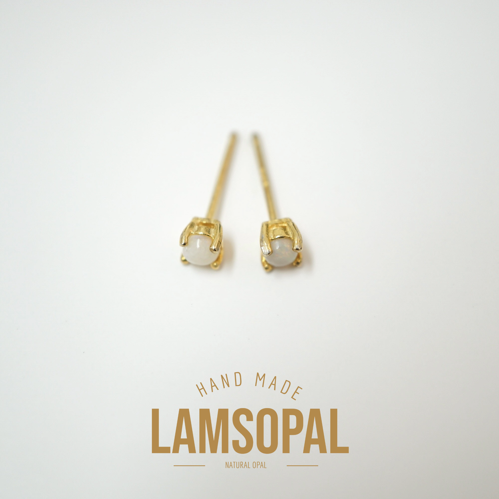 A pair of gold post earrings with oval white opal gemstones, displayed on a clean white background with a gold 'LAMSOPAL' brand logo and 'HAND MADE' text below.