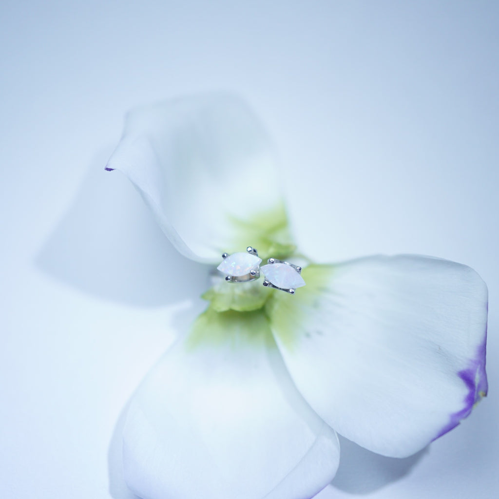 A delicate silver ring with two clear gemstones set in a floral setting, nestled among white flower petals on a soft, light blue background.