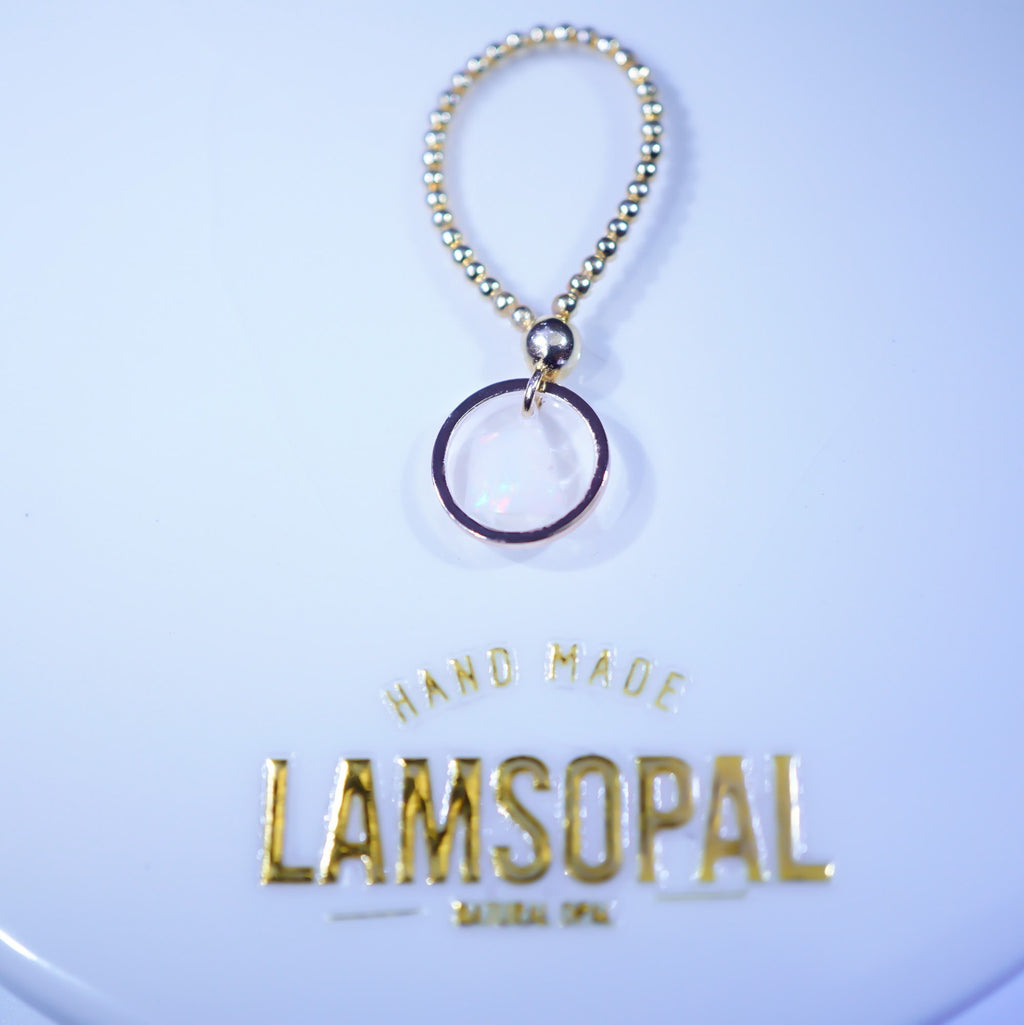 A gold beaded keychain or bag charm with a circular ring pendant, displayed above a branded gold 'LAMSOPAL HAND MADE' label on a light blue background.
