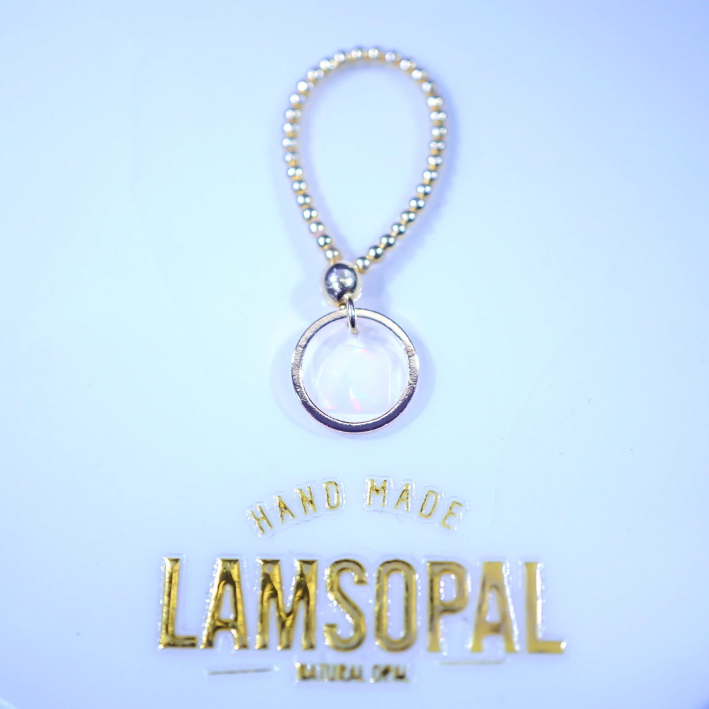 A handmade keychain or bag charm featuring a silver-toned beaded loop and a silver-rimmed circular pendant with a milky white iridescent center, displayed against a light blue background with gold 'LAMSOPAL' branding text below.