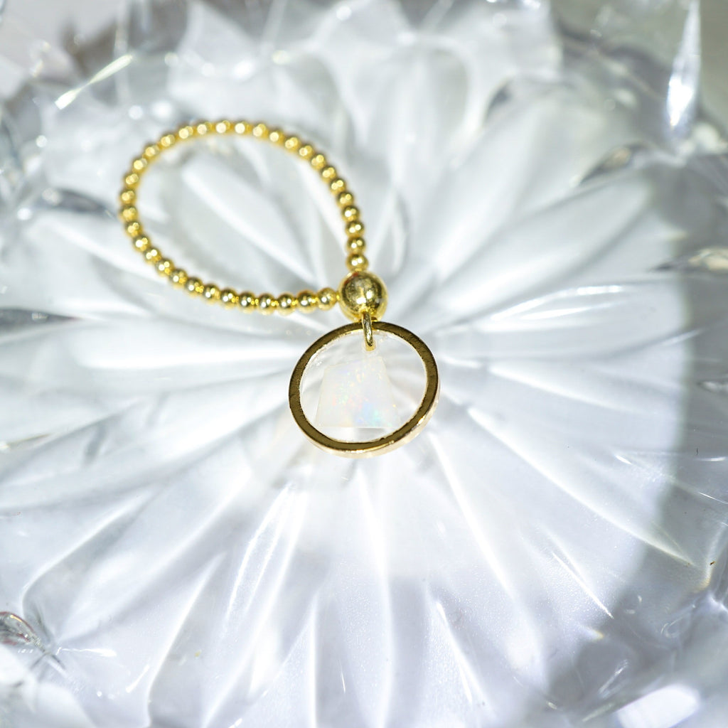 A gold-toned beaded bracelet with a single flat circular ring charm, displayed on a textured white surface.