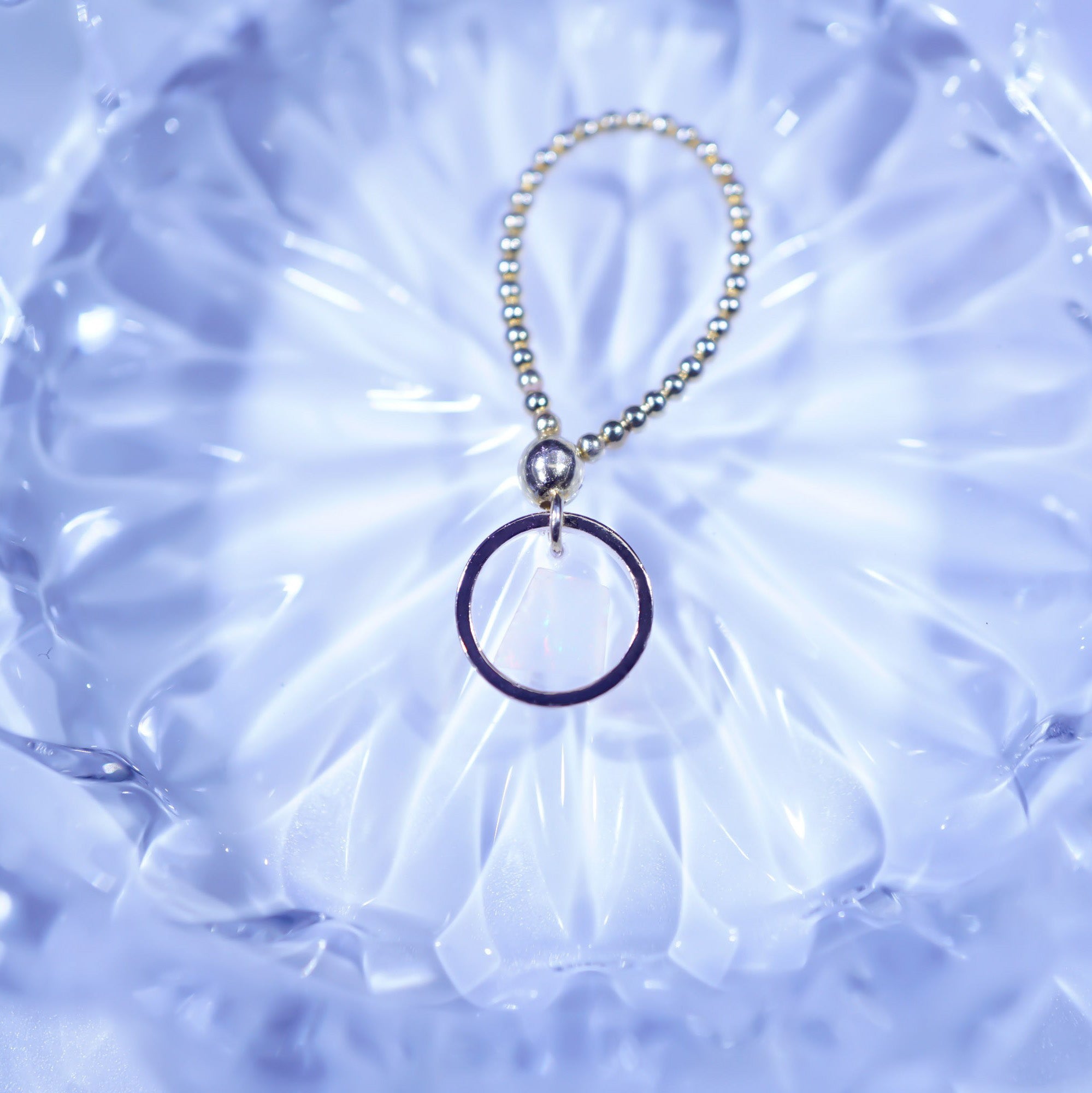 A silver beaded keychain with a single thin dark ring pendant, displayed on a textured, light blue glass plate.