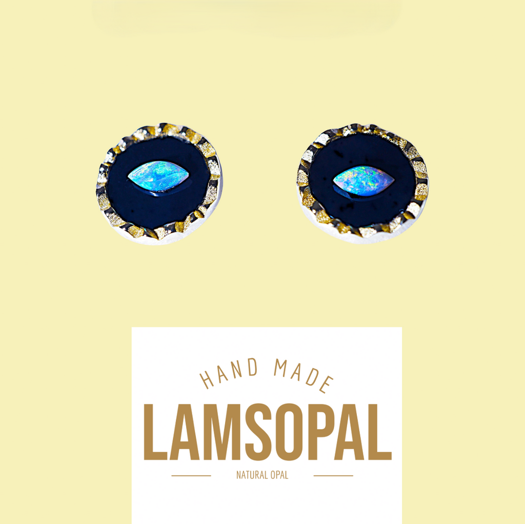 A pair of handmade Lamsopal natural opal stud earrings with a dark blue center and a gold-rimmed bezel, shown above a white label with the brand name 'LAMSOPAL' on a pale yellow background.
