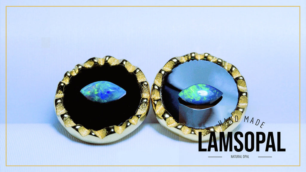 A pair of Lamsopal hand-made natural opal earrings with marquise-cut iridescent opal centers set in gold-toned bezel settings with black inlay, shown on a light blue background with a gold border.