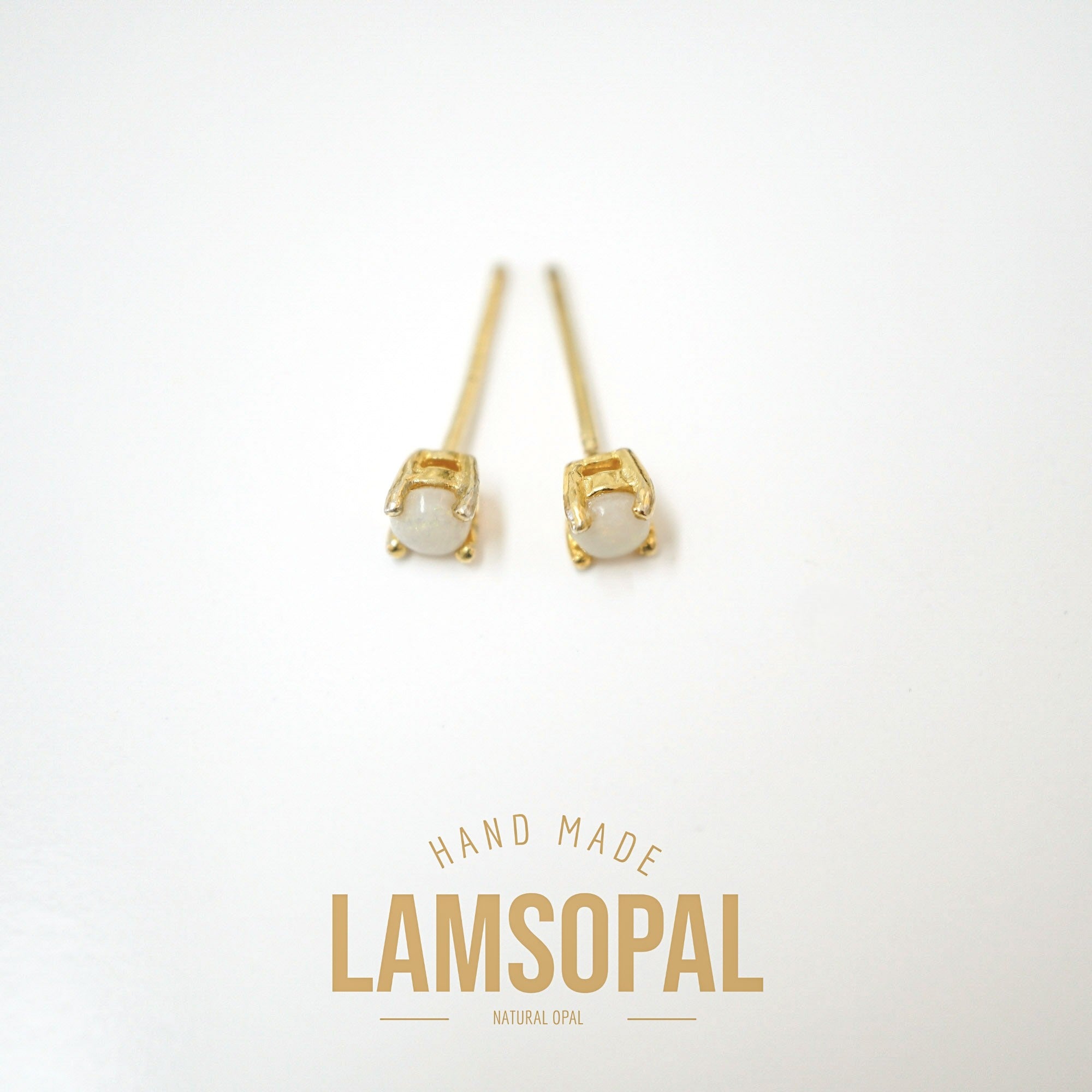 A pair of gold stud earrings with oval white natural opal stones, displayed on a clean white background with a gold 'LAMSOPAL' brand logo at the bottom.