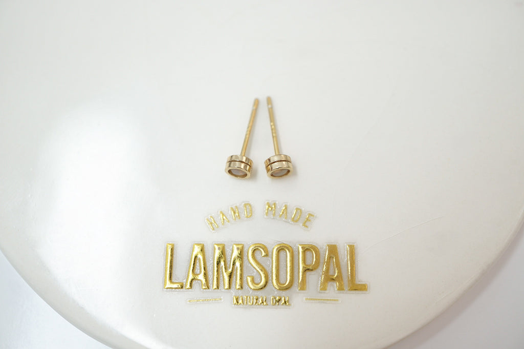 A pair of small gold-toned stud earrings displayed on a white oval surface with the brand name LAMSOPAL printed in gold below.