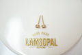 A pair of small gold-toned stud earrings displayed on a white oval surface with the brand name LAMSOPAL printed in gold below.
