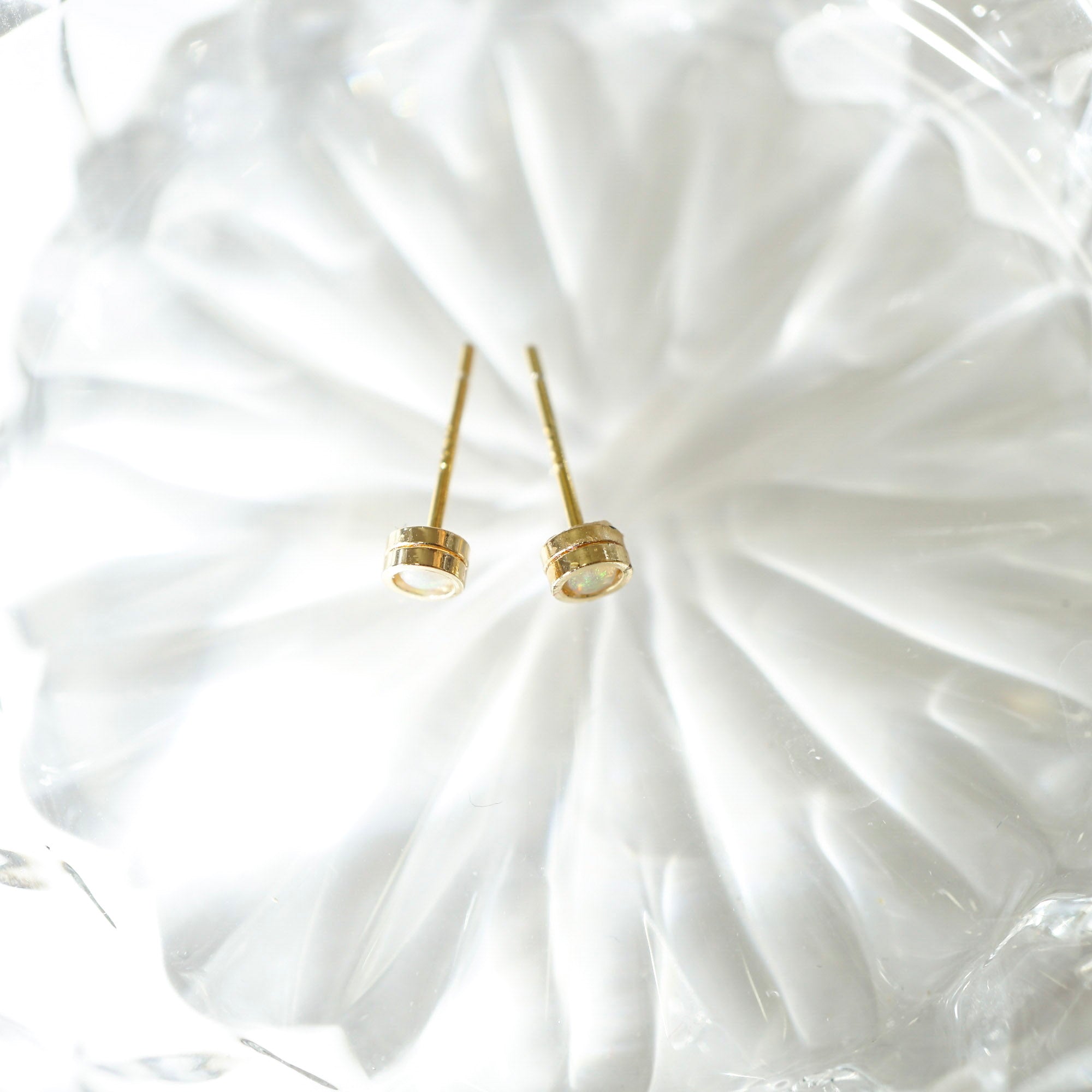 A pair of gold post earrings with textured circular disc tops, resting on a white textured glass plate.