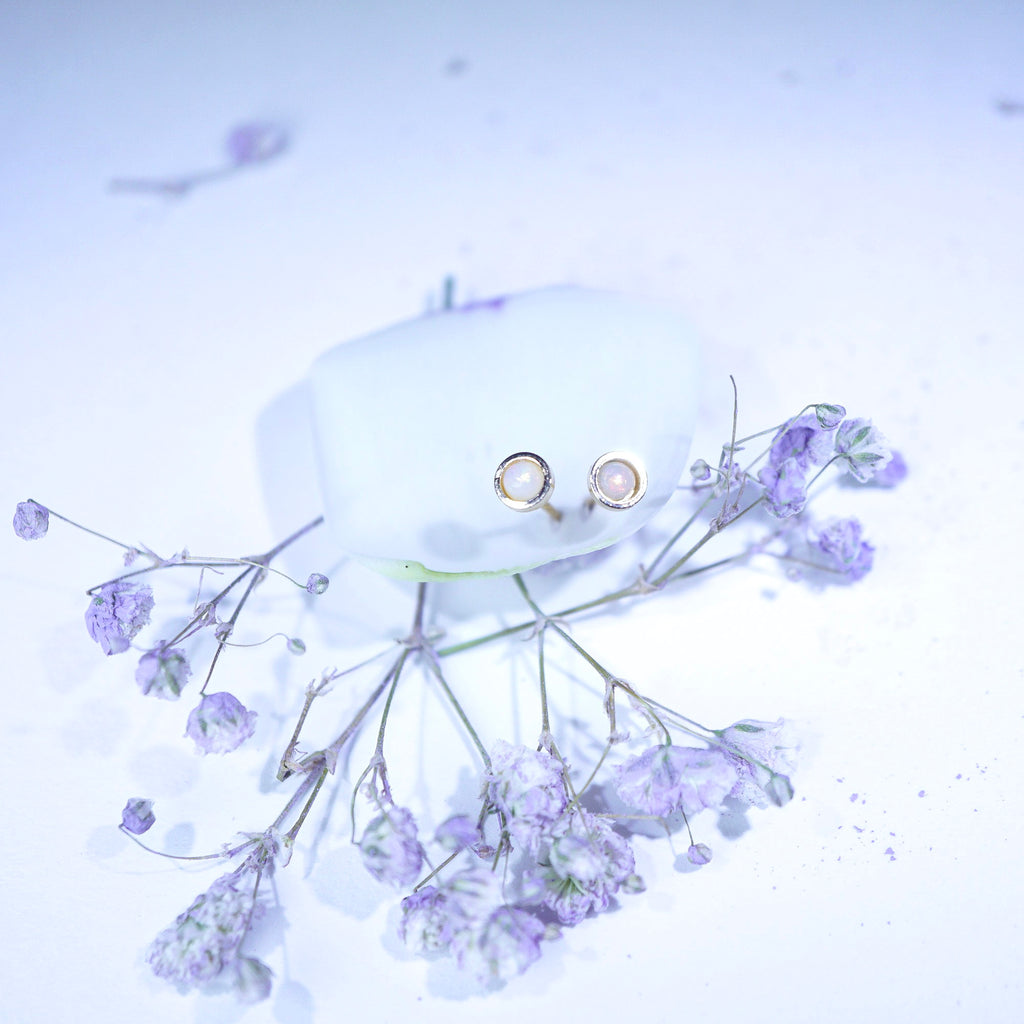 A pair of small gold hoop earrings with clear stones, displayed on a white surface with dried lavender flowers around them.