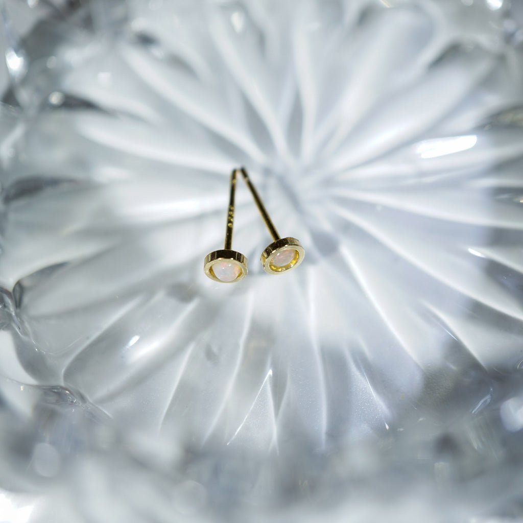 A pair of gold post earrings with oval milky white stones, resting on a textured, faceted clear glass surface.